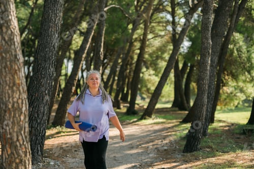 Preview: Old woman with dreadlocks walking with her mat to yoga or pilates class in park copy space - well