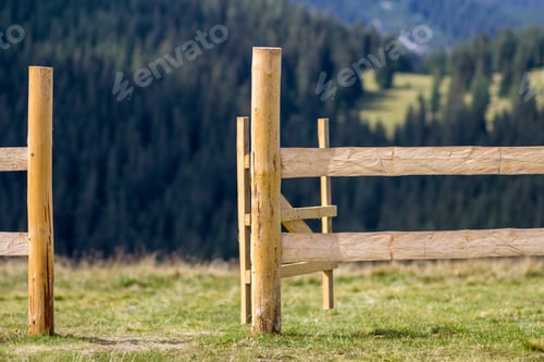 Preview: Close-up of low rough wooden fence on lit by bright summer sun grassy valley on Carpathian mountains