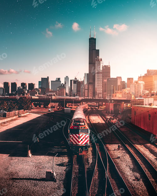 Preview: Vertical shot of a train on rails near skyscrapers under a blue sky during sunset in a city