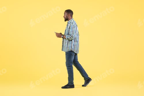 Preview: African Guy Using Application On Phone Walking On Yellow Background