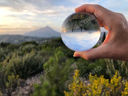 Preview: View through a crystal ball over countryside and wildflowers to a mountain on the horizon