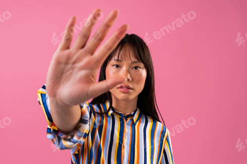 Preview: Beautiful asian woman portrait, asian woman showing stop gesture against pink background