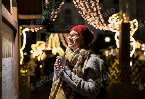 Preview: Young woman holding cup by decorated stall at Christmas market