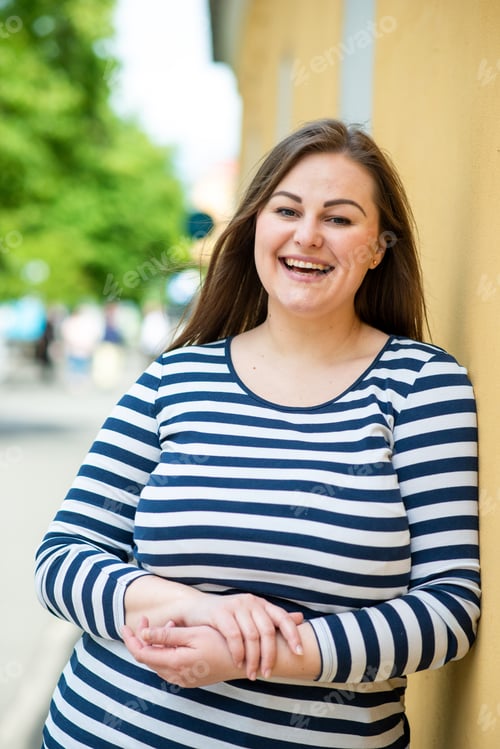 Preview: A beautiful, sweet, smiling lady leaned against an orange wall outdoors