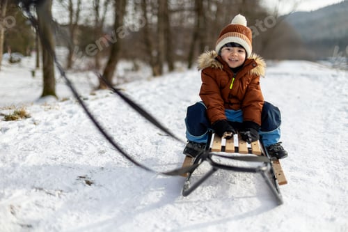 Preview: Happy child rides a sled along a snow-covered path during a frosty winter