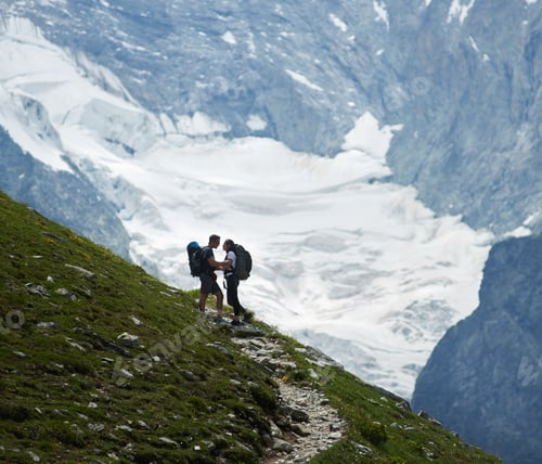 Preview: Romantic couple standing on a green meadow at rocky background of Swiss Alps
