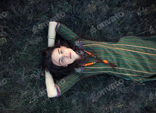 Preview: Beautiful hippie woman lying on grass relaxing on summer field