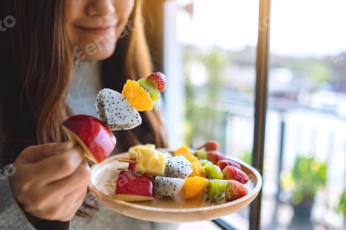 Preview: Closeup image of an asian woman holding and eating a fresh mixed fruits on skewers