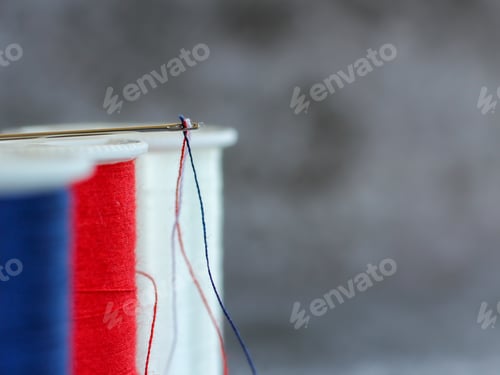 Preview: Sewing thread in United States colors through the eye of the needle closeup view with copy space