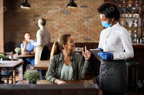 Preview: Happy woman making an order while talking to black waitress in a cafe.