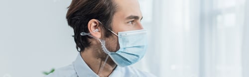 Preview: security man in medical mask and earphones looking away in office, banner