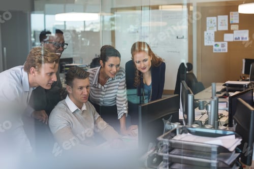 Preview: Businessman discussing with colleagues while working on computer seen through glass