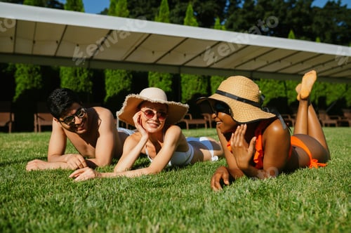 Preview: Cheerful friends rest on the grass near the pool