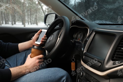 Preview: Young man with coffee and smartphone inside car, closeup