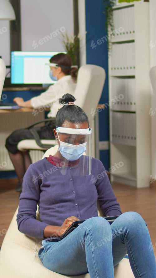 Preview: African employee holding tablet sitting on armchair in office room