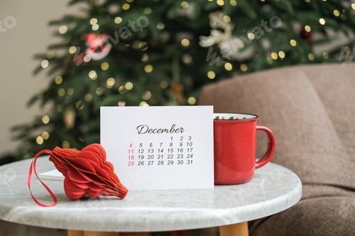 Preview: December calendar, red mug and red Christmas decorations on table with Christmas tree in background