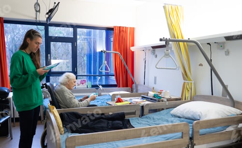 Preview: Senior woman in wheelchair in hospital room and visiting woman