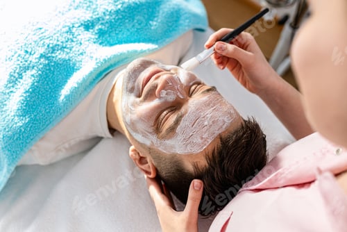 Preview: Beautician doing face treatment in beauty salon to a man.