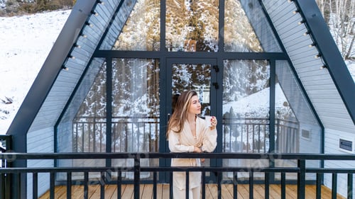 Preview: Woman standing on the balcony of A Frame cabin in the winter park