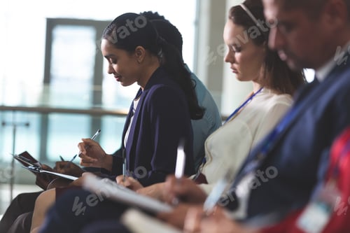 Preview: Business people writing on notepads in business seminar in modern office building