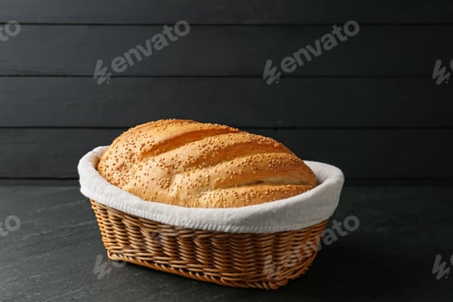 Preview: Loaf of bread with sesame seeds in basket on black textured table