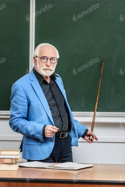 Preview: grey hair professor pointing on something at blackboard with wooden pointer