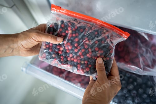 Preview: Man hand taking frozen lingonberry, blueberry mix in bag from freezer. Stocking up for winter, diet