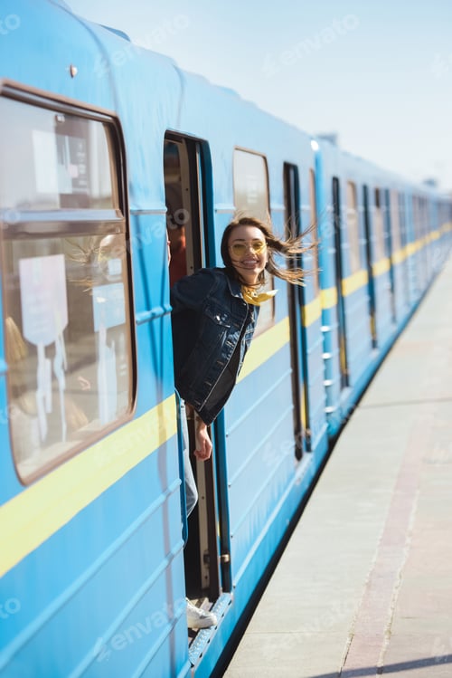 Preview: smiling stylish woman in sunglasses looking out from train at outdoor subway station