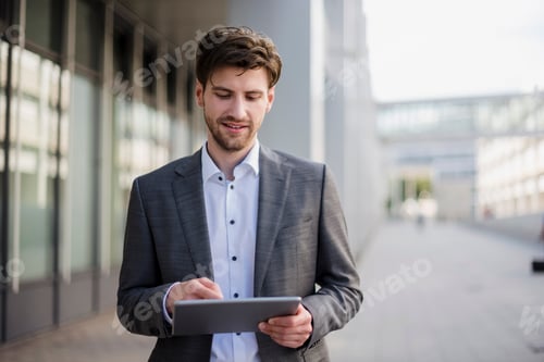 Preview: Smiling businessman in the city using tablet
