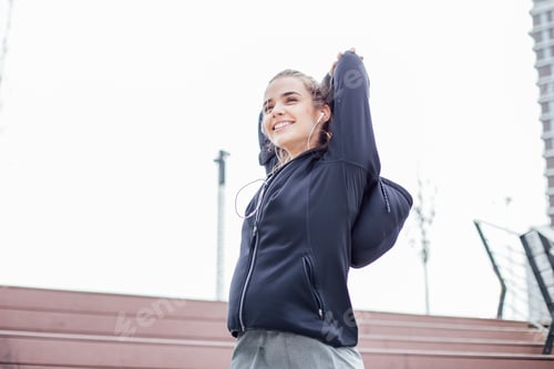 Preview: Fit young woman with earphones doing stretching exercises on stairs outdoors