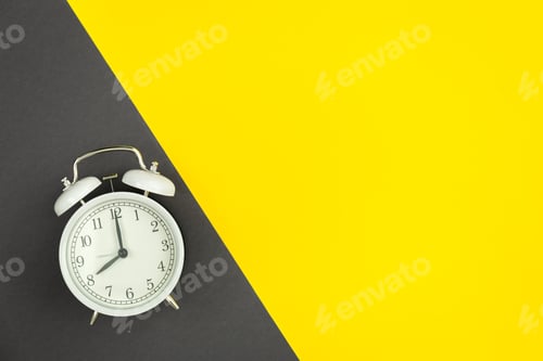 Preview: White alarm clock on a yellow and green background, flat lay.
