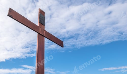 Preview: Old rusty metal cross against a blue sky with white clouds