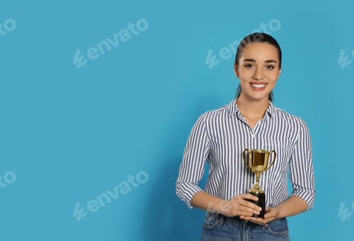 Preview: Portrait of happy young woman with gold trophy cup on blue background, space for text
