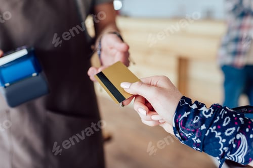 Preview: cropped shot of client giving credit card to waiter holding payment terminal in cafe