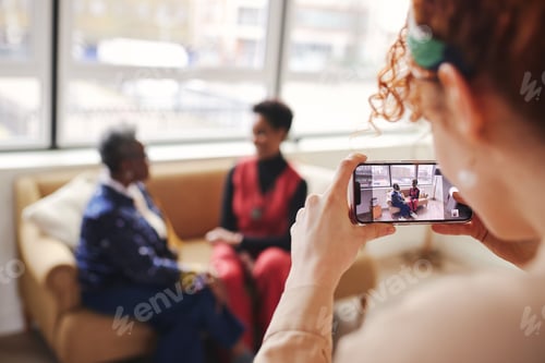 Preview: Woman taking photo of two black colleagues on smartphone, image on digital screen