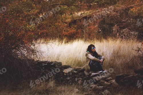 Preview: Millenial woman sitting on a fence. Stone. Reflection and thought. Autumn colors. Earth tone.