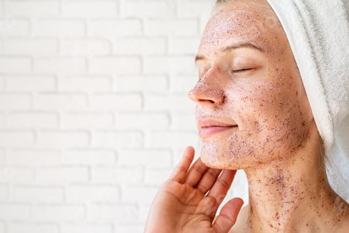 Preview: Happy smiling young woman in white bath towels applying scrub on her face