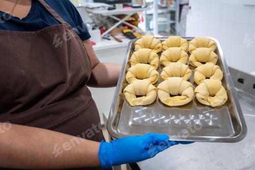 Preview: Baker holding raw croissants on baking tray