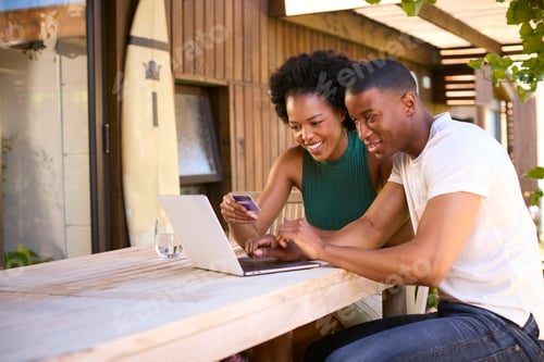 Preview: Excited Couple With Credit Card Using Laptop At Home To Book Holiday Or Shop Online