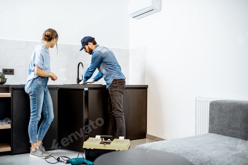 Preview: Plumber repairing kitchen faucet with woman in the apartment