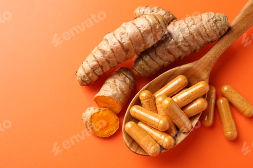 Preview: Turmeric rhizomes, capsules and spoon on orange background, flat lay. Space for text