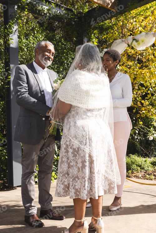 Preview: Happy biracial female marriage officiant and senior couple during wedding in sunny garden