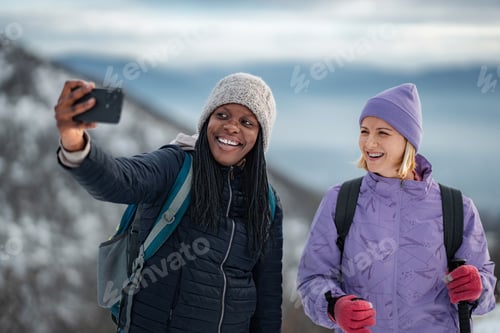 Preview: Happy young women friends taking selfie on winter mountain hike