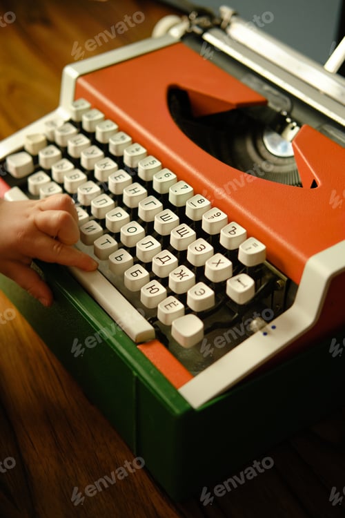 Preview: Children's hand presses space bar on orange vintage typewriter and wants to make pause. Child learns