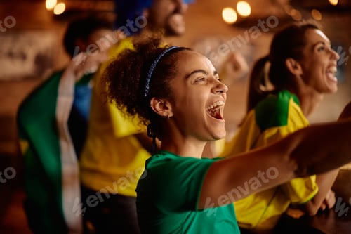 Preview: Cheerful sports fan watching a match with her friends in pub.