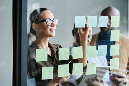 Preview: Young female manager making notes on notepaper on transparent board