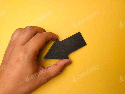 Preview: Hand holding wooden black arrow with copy space on a yellow background.