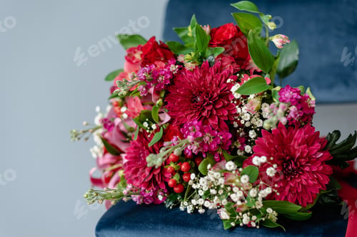 Preview: Bunch of flowers in burgundy tones on a dark blue velvet chair.