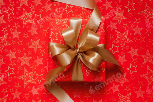 Preview: Red Christmas gift with golden ribbon and bow on red background decorated with golden stars pattern.