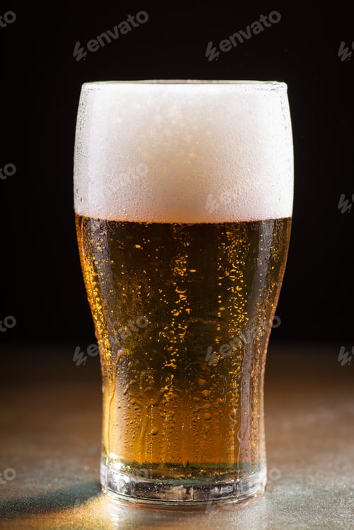 Preview: Vertical shot of a glass of cold refreshing beer with foam on a wooden table